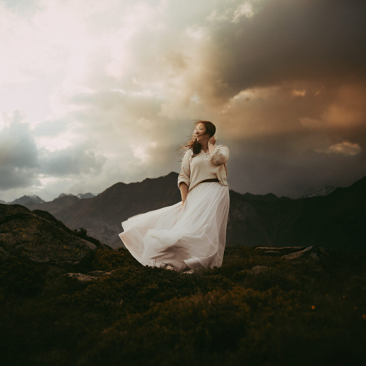 Frau steht vor Bergkulisse in wehendem Rock